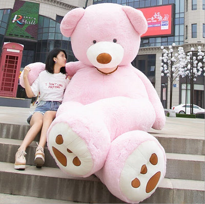 Large soft leather teddy bear toy in pink sitting outdoors next to a woman on stone steps