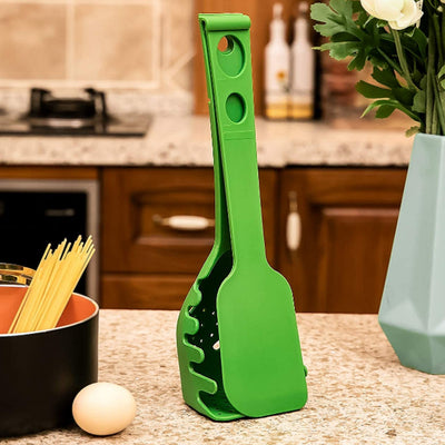 Green versatile kitchen spoon for pasta and eggs standing on kitchen counter near pot and egg